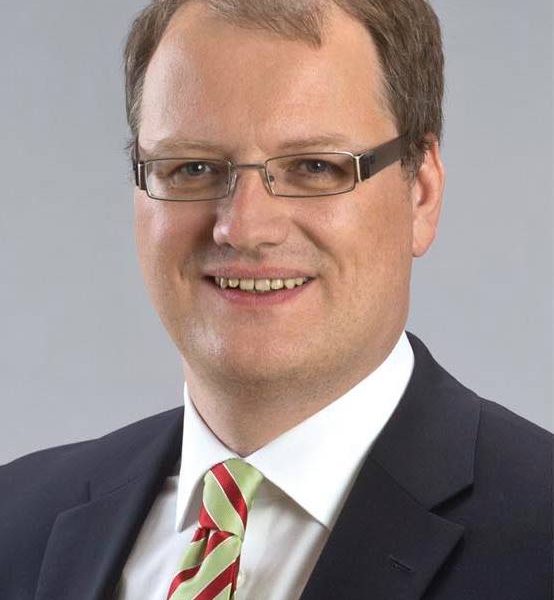 Porträtfoto von Olaf Schade vor grauem Hintergrund