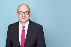 Porträtfoto von Andre Stinka vor hellblauem Hintergrund