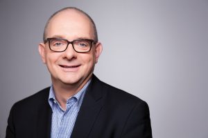 Porträtfoto von Andre Stinka vor grauem Hintergrund