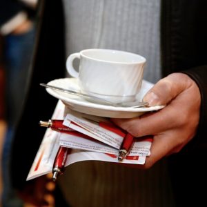 Ein Teilnehmer hält eine Kaffeetasse und Flyer