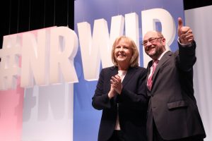 Hannelore Kraft und Martin Schulz stehen lächelnd Arm in Arm vor einer #NRWIR-Bühne
