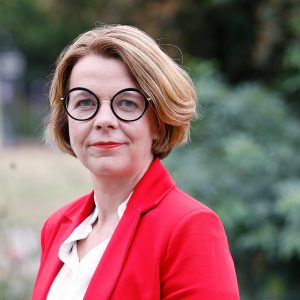 Porträtfoto von Nadja Lüders. Sie trägt ein weißes Hemd und ein rotes Jackett.