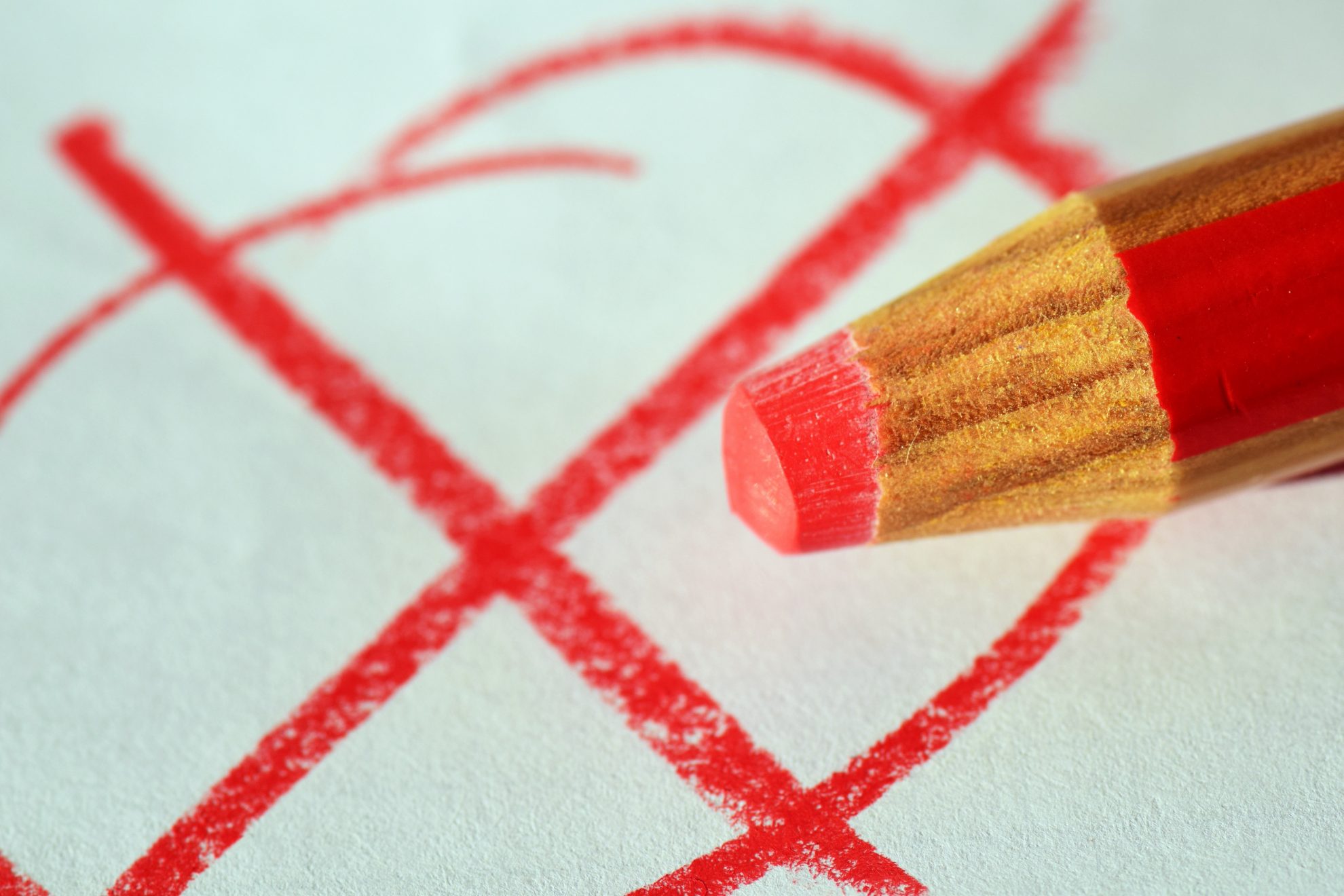 Roter Buntstift vor einem weißen Blatt Papier, auf dem ein roter Kreis mit einem roten Kreuz aufgemalt ist