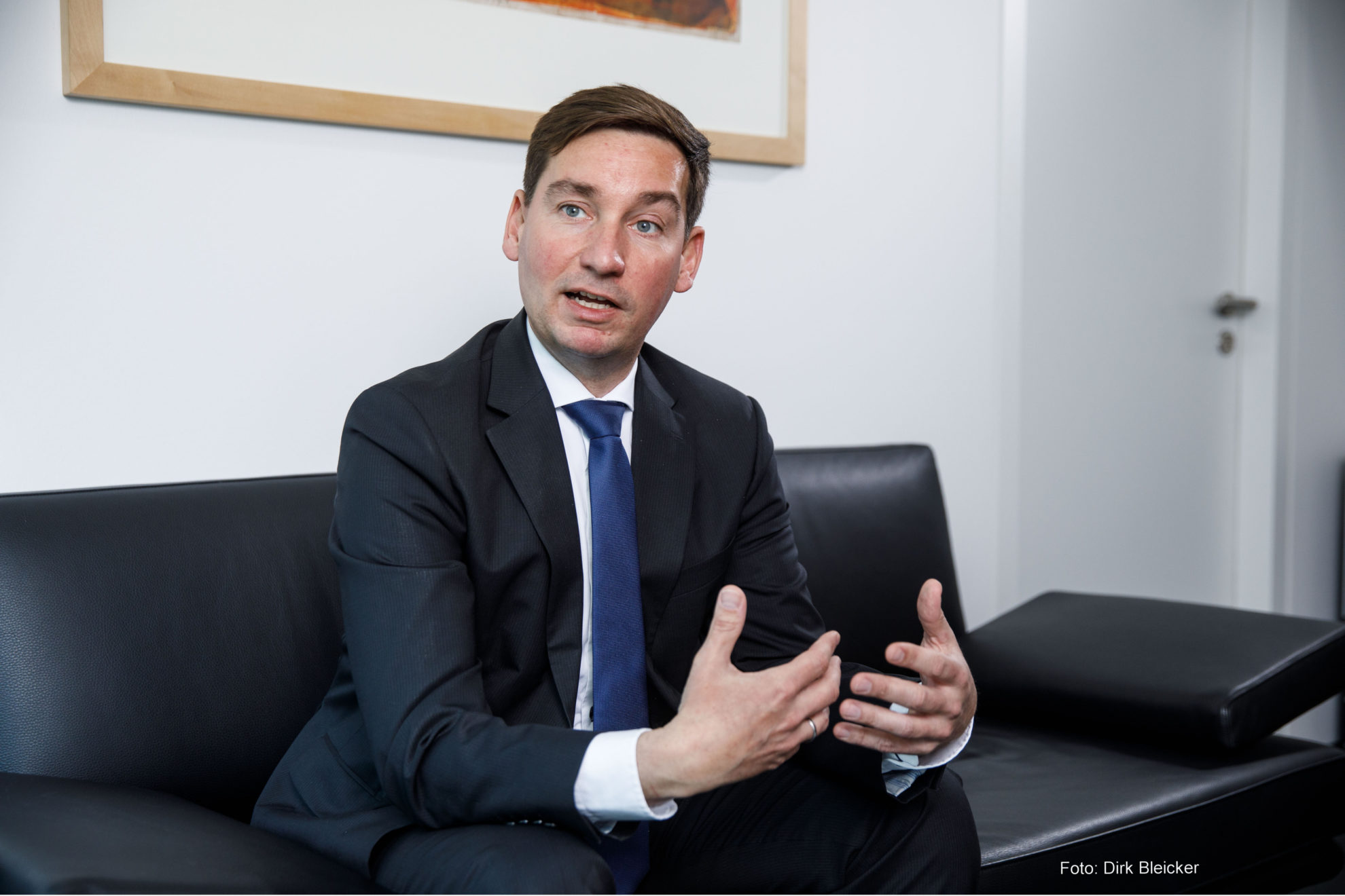 Sebastian Hartmann, NRWSPD-Vorsitzender, sitzt in einem dunklen Anzug gekleidet auf einer dunklen Couch, redet und bewegt dabei die Hände